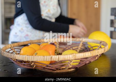 Im Vordergrund befindet sich ein Gericht mit leuchtenden Früchten, im Hintergrund legt eine Frau Früchte auf einen Teller Stockfoto