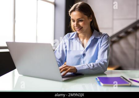 Junge, schöne Frau arbeitet als Freiberuflerin von zu Hause aus für einen Computer mit einem Laptop auf einem weißen Schreibtisch Stockfoto