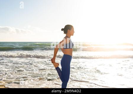 Weibliche Schwimmerin, die am Strand steht und ein Bein streckt Stockfoto