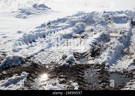 Schmelzen von Schnee und Schlamm mit Autoreifen auf einer unbefestigten Straße, die von den Strahlen der hellen Sonne erleuchtet wird. Stockfoto