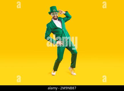 Ein lustiger, stylischer Mann in grüner Kleidung feiert St. Patrick's Day auf orangefarbenem Hintergrund. Stockfoto