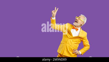 Porträt eines fröhlichen, grau-haarigen Mannes mit doppeltem V-Zeichen isoliert auf leuchtend leuchtendem, leuchtend leuchtenden, violetten Hintergrund. Stockfoto