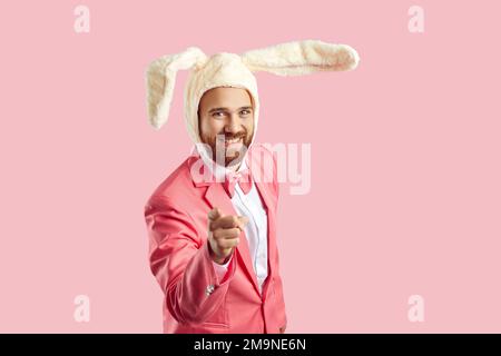 Ein glücklicher junger Mann mit lustigen Osterhäschen-Ohren, der lächelt und mit dem Finger auf die Kamera zeigt Stockfoto