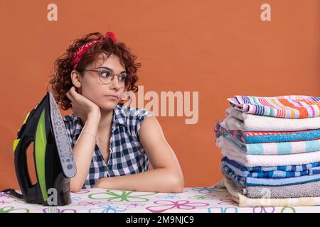 Ein Mädchen mit Brille blickt auf ein paar gebügelte Handtücher. Lockiges Haar. Stockfoto