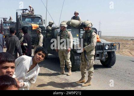 Bewaffnete Marines des US Marine Corps (USMC), die der 24. Service Support Group (SSG), der 24. Marine Expeditionary Unit (MEU), Special Operations Capable (SOC) zugewiesen sind, verwenden ein M998 High-Mobility Multipurpose Wheeled Vehicles (HMMWV) und zwei Medium Tactical Vehicle Replacement (MTVR) Trucks; Einrichtung einer Absperrung, während sich lokale irakische Zivilisten während der Operation "IRAKISCHE FREIHEIT" versammeln, um ein Bauprojekt entlang einer großen Straße in Al Rifa, Irak, zu beobachten. Operation/Serie: IRAKISCHE FREIHEITSBASIS: Al-Rifa-Land: Irak (IRQ) Stockfoto