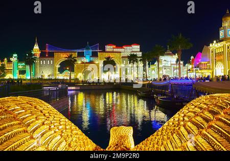 DUBAI, Vereinigte Arabische Emirate - 6. MÄRZ 2020: Die Skulptur des Goldenen Adlers auf der Brücke vor dem dunklen Wasser des Kanals und der Pavillons des Global Village Dubai, auf Mar Stockfoto