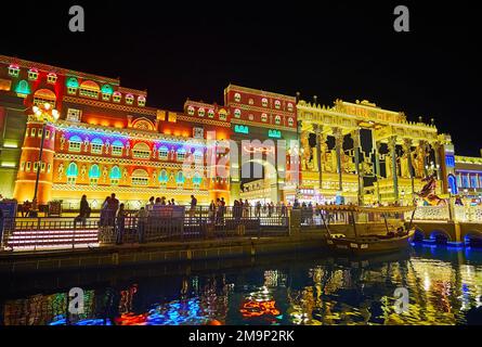 DUBAI, Vereinigte Arabische Emirate - 6. MÄRZ 2020: Wunderschöne beleuchtete Pavillons des Global Village Dubai hinter dem Kanal mit verankertem hölzernen Touristenboot, am 6. März Stockfoto