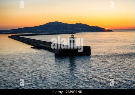 Blick auf den Sonnenuntergang am Wellenbrecher und den South Stack Mountain in Holyhead, Anglesey. Stockfoto