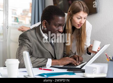 Frau Büroleiterin, die Männern hilft, während sie am Laptop arbeitet Stockfoto