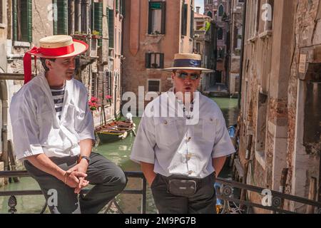 Zwei Gondoliere, gekleidet in der traditionellen Uniform eines Gondoliers, machen Mittagspause auf einer Brücke über einem Kanal in Venedig, Italien. Stockfoto