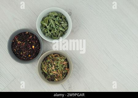 Verschiedene Kräutertees in Schüsseln auf hellem Holzhintergrund. Aromatische Blätter. Draufsicht. Stockfoto