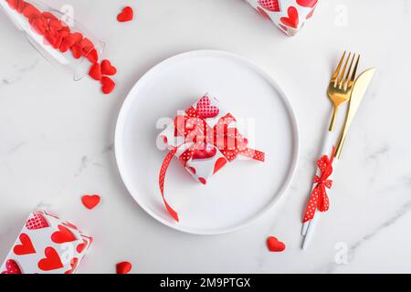Hintergrund für das Valentinstag-Abendessen mit Geschenken, roten Herzen, Gabel und Messer auf weißem Marmor. Romantische Festtagstische Stockfoto