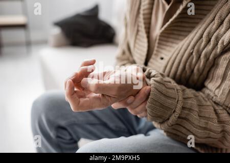 Teilansicht eines älteren Mannes mit Parkinsonismus, der zitternde Hand hält, während er zu Hause sitzt, Stockbild Stockfoto