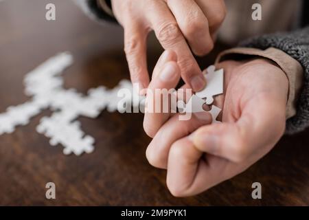 Teilansicht eines alten Mannes mit parkinson-Syndrom, der Puzzleelemente in zitternden Händen hält, Stockbild Stockfoto