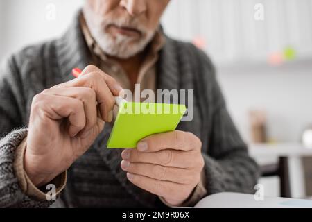 Zugeschnittene Ansicht eines verschwommenen Mannes mit Gedächtnisverlust und Schreiben auf Haftnotizen mit Filzstift, Stockbild Stockfoto