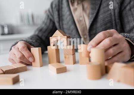 Abgeschnittene Ansicht eines älteren Mannes, der an alzheimer-Syndrom leidet und zu Hause mit Holzblöcken spielt, Stockbild Stockfoto