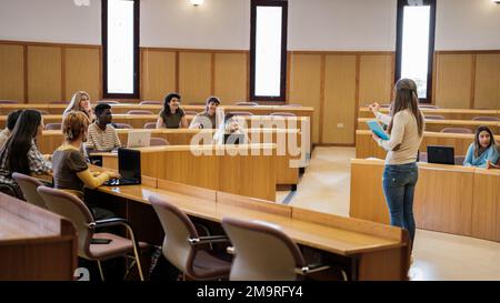 Gruppe von Universitätsschülern in einem kreisförmigen Unterrichtsraum, die sich mit den Erläuterungen des Lehrers befassen- Bildungskonzept, multikulturelles und naturwissenschaftliches Konzept Stockfoto