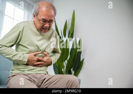 Asiatischer Seniorenmann, der auf dem Sofa sitzt und unter Magenschmerzen leidet Stockfoto