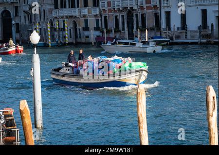 Zwei Männer steuern ein Boot voller Müll, der früh am Morgen von den Straßen Venedigs abgeholt wurde, um es aus der Hauptlagune zu bringen. Stockfoto