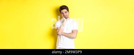 Gelangweilter und unamüsiert Mann, der mit Gleichgültigkeit schaut, in weißen Kleidern über gelbem Hintergrund stehend Stockfoto