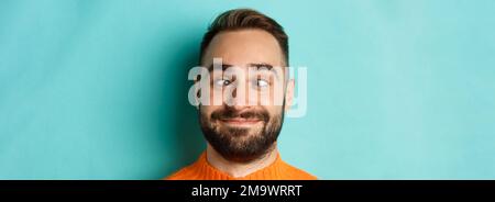 Kopfbild des lustigen kaukasischen Mannes, der Gesichter macht, schielend und lächelnd dumm, über hellblauem Hintergrund stehend Stockfoto