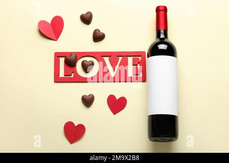 Eine Flasche Wein, WORTSCHATZ, Schokoladenbonbons und Papierherzen auf beigefarbenem Hintergrund. Valentinstag-Feier Stockfoto