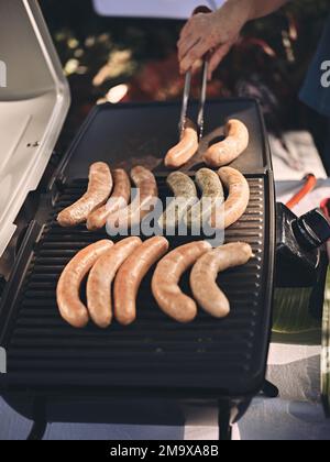 Frische Würstchen und Hot Dogs grillen draußen auf einem Gasgrill. Konzeptpicknick Stockfoto