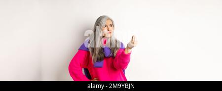 Mürrische asiatische Großmutter beschwert, zeigt italienisch, was Sie wollen Geste, schüttelt die Finger und starrte wütend links auf den Kopierraum, über stehen Stockfoto