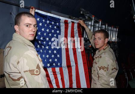 STAFF Sergeant der US Air Force (USAF) (SSGT) Kevin Lucas (links) und SENIOR AIRMAN (SRA) Donald Cook (rechts), beide mit dem 407. Expeditionary Communications Squadron (EQCS), RAF (Royal Air Force) Mildenhall, England (eng), Hängen Sie eine US-Flagge an Bord eines C-130-Frachtflugzeugs von Hercules auf, zum Gedenken an einen gefallenen FLIEGER aus ihrer Einheit, der bei der Unterstützung der IRAKISCHEN FREIHEIT starb. Diese US-Flagge wird vom Luftwaffenstützpunkt Tallil (ab), einer Provinz Nasiriyah, Irak (IRQ), zurück in die Vereinigten Staaten geflogen, um an die Familie der gefallenen Airmans geliefert zu werden. Stützpunkt: Luftwaffenstützpunkt Tallil Staat: DHI Qar Land: Irak (IRQ) Stockfoto