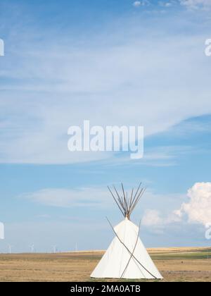 Weißer Tipi oder Tipi im Vordergrund mit Windturbinen in der Ferne. Fotografiert im First Peoples Buffalo Jump State Park in Montana. Stockfoto