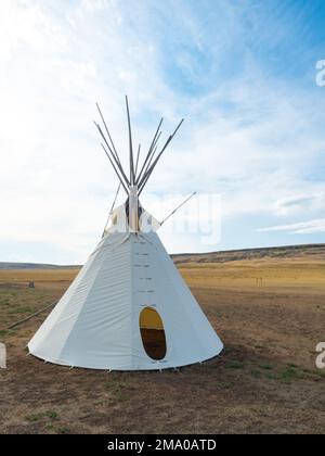 Weißes Tipi oder Tipi im Vordergrund mit einem früheren Büffelsprung im Hintergrund. Fotografiert im First Peoples Buffalo Jump State Park in Mont Stockfoto