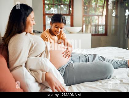 Schwangere mutter und neugieriges Kind auf dem Bett berühren den Bauch mit einem erregten, fröhlichen und fröhlichen Lächeln. Indische Familie und Kind warten auf Baby, Geschwister und Beziehung Stockfoto