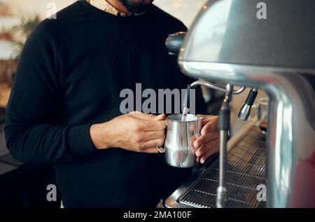 Hände, Mann und Barista brühen Kaffee im Café mit einer Maschine für heißes Getränk, Koffein oder Dampf. Hand eines männlichen Mitarbeiters, der Milch in einem Metallkrug aufschäumt Stockfoto