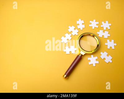 Lupe sucht fehlendes Puzzle auf gelbem Hintergrund Stockfoto