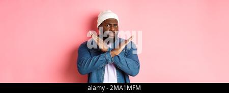 Enttäuscht Schwarzer Mann, starrte auf Kamera unzufrieden und runzelte die Stirn, zeigt Stop Cross Geste, verbieten und nicht einverstanden, stehen über rosa Hintergrund Stockfoto