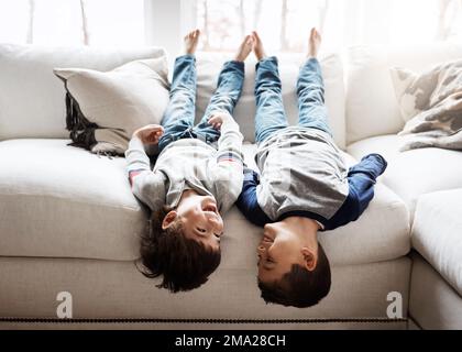 Kinder, die kopfüber spielen und mit ihrer Familie zu Hause Spaß haben, mit Geschwistern, Brüdern auf dem Sofa und im Wohnzimmer entspannen. Glückliche Menschen, Liebe und Qualität Stockfoto