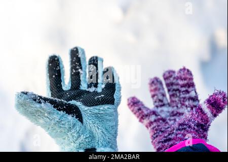 Ein Paar unpassender Handschuhe an einem Kind, das über einem weißen Schneehintergrund gehalten wird Stockfoto