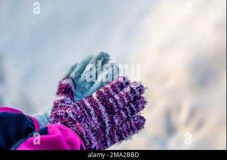 Ein Paar unpassender Handschuhe an einem Kind, das über einem weißen Schneehintergrund gehalten wird Stockfoto