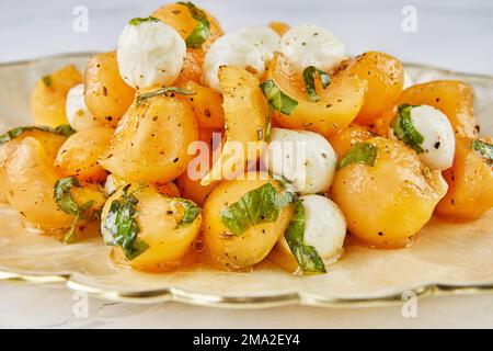 Salat mit Melonenbechern, Babymozzarella und Kräutern auf weißem Marmor. Schließen. Stockfoto