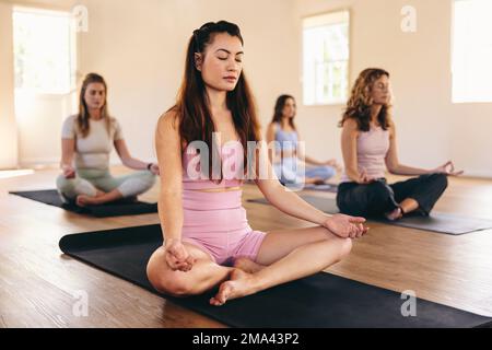 Eine Gruppe verschiedener Frauen, die Sukhasana-Meditation in einem Yogakurs praktizieren. Frauen unterschiedlichen Alters, die Atemübungen in einem Yoga-Studio machen. Sportlicher Stil Stockfoto