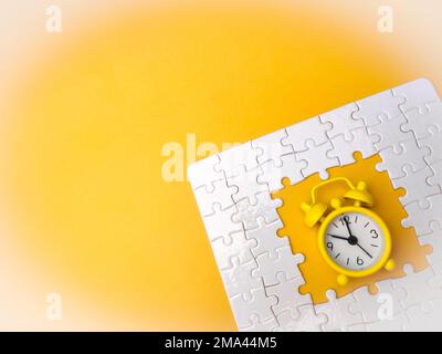 Konzept mit gelbem Wecker und Puzzle auf gelbem Hintergrund Stockfoto