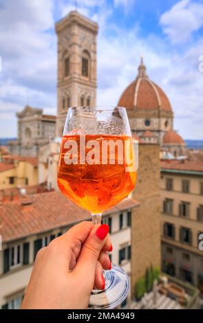 Eine Frau hält einen Aperol Spritz Cocktail mit Blick auf den Dom oder die Cattedrale di Santa Maria del Fiore in Florenz, Italien Stockfoto