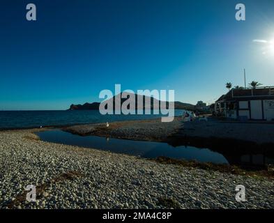 Kieselstrand des Ortes Altea an der weißen Küste mit dem Berg im Hintergrund unter einem wunderschönen sonnigen blauen Himmel an einem Herbsttag. Stockfoto