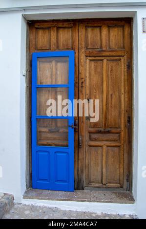Große braune Holztür eines Hauses im kleinen Dorf Altea in Alicante mit einer weiteren kleineren Tür vorne in blau gestrichen. Stockfoto