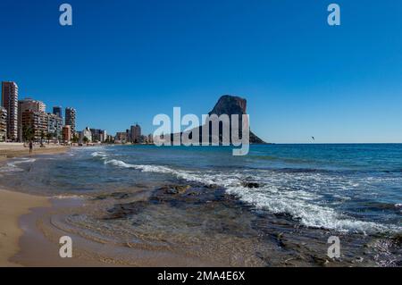 Panoramablick auf die Stadt Calpe mit ihren Gebäuden und Ifach-Felsen im Hintergrund mit den Wellen, die am Ufer des Strandes enden Stockfoto