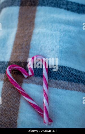 Einsames Herz des Valentinstages mit weihnachtlichen Zuckerstangen auf einer warmen Decke an einem kalten Wintertag. Stockfoto
