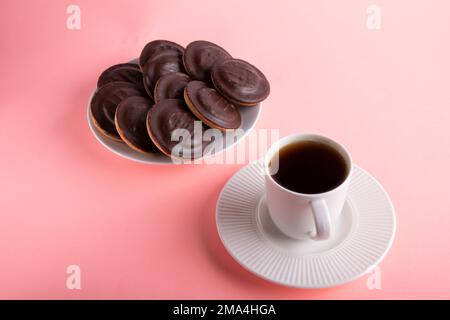 Schokoladenkekse auf einem Teller mit Glasur und eine Tasse Kaffee auf einer Untertasse Stockfoto