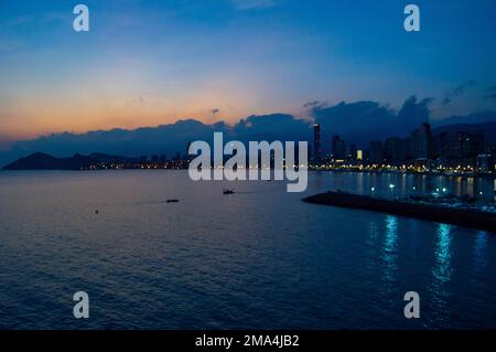 Panoramablick auf die Stadt Benidorm bei Sonnenuntergang mit allen Lichtern der Hotels und der Promenade mit Wolken im Hintergrund am Himmel. Stockfoto
