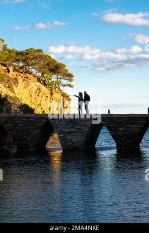 Zwei Männer weisen auf die Landschaft hin, die man im Hintergrund auf der Brücke sehen kann, die zur Insel in Cadaques führt. Stockfoto