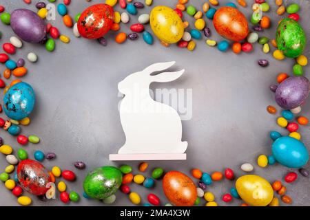 Farbenfrohe Ostereier, Schokoladen-Ostersüße und Häschen auf grauem Hintergrund. Draufsicht mit Kopierbereich. Festliches Osterkonzept. Stockfoto